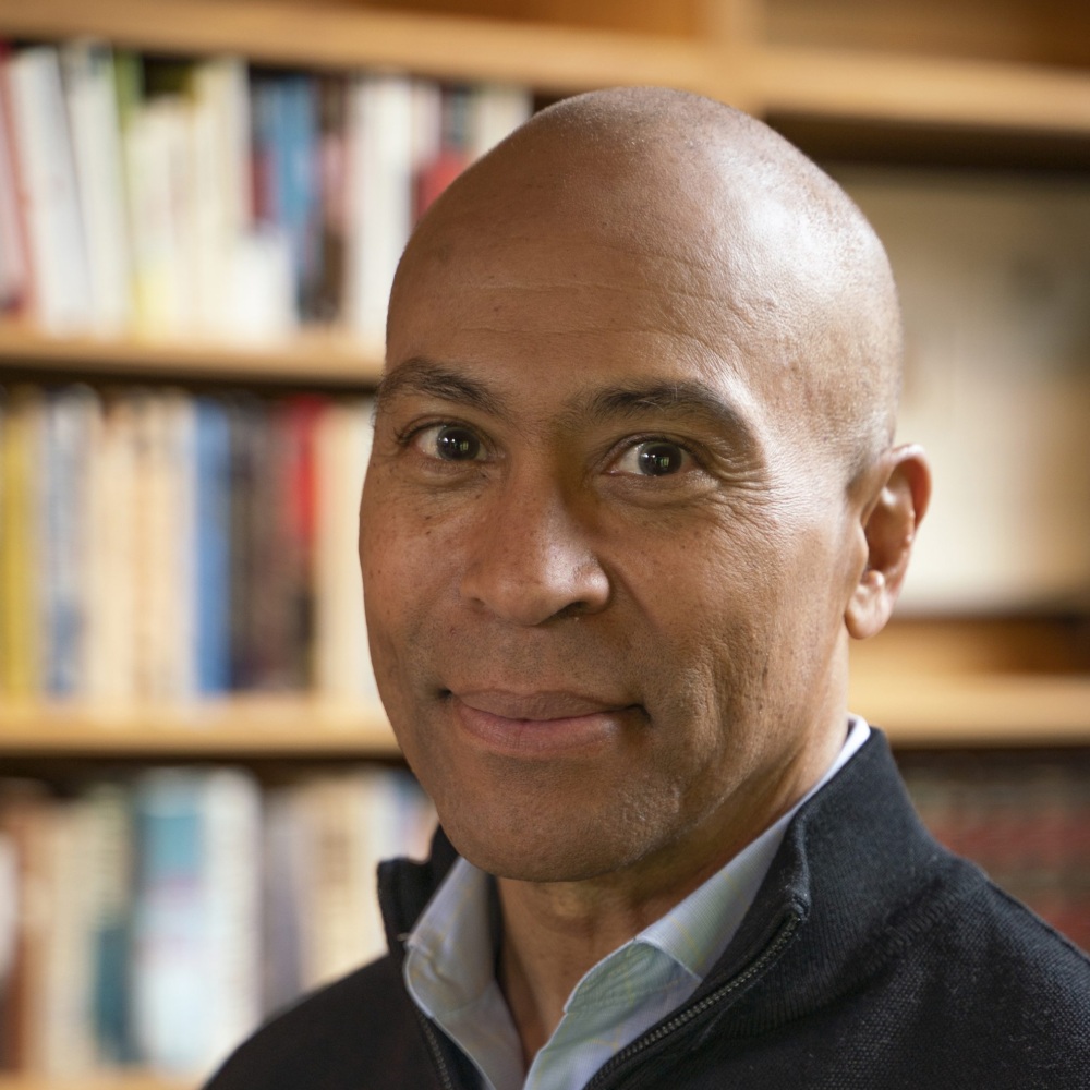 Headshot of Deval Patrick, wearing a quarter zip in a library.